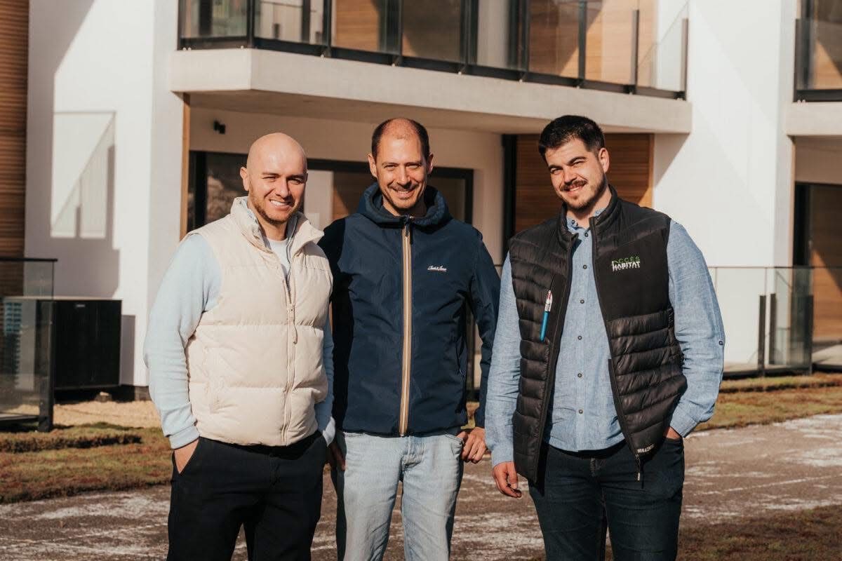 acc_article Accès Habitat Three men stand outside a modern white building, smiling at the camera with hands in pockets.
